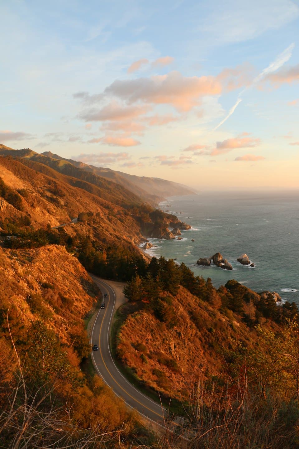 Cars drive on a coastal road at sunset.