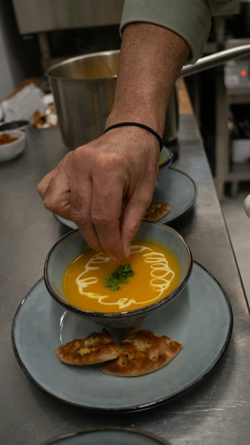 Hands add fresh green herbs to a bowl of soup.